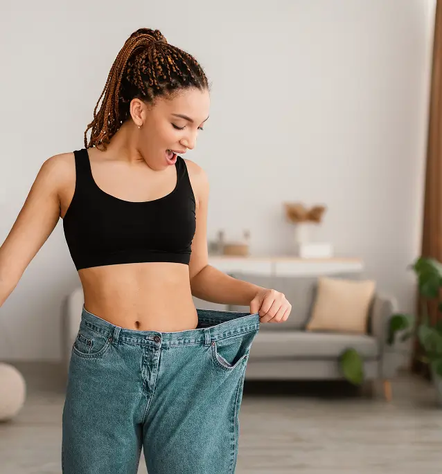A woman happily shows off her loose jeans after weight loss.